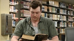 student seated in library reading old book