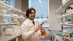 oliver loreto at a campus lab bench, holding a lit blowtorch and smiling