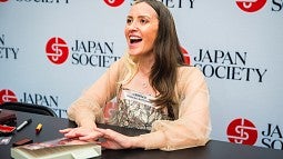 natalie jacobsen signing copies of her novel at a table with a wall of "japan society" logos behind her