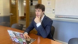 student in suit seated at seminar table on laptop