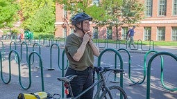 larissa stiglich buckling on her helmet standing at bike on campus
