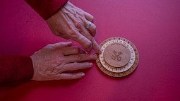 hands using a wooden cipher wheel on a red table
