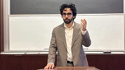 parsa aghel standing at a lecture hall podium, speaking and gesturing