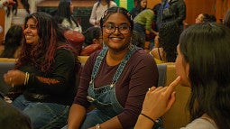 student smiling at another student in a crowded, lively room of students engaging with one another