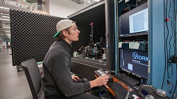 student seated at a large piece of science equipment, typing on a keyboard and reading a screen