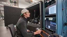 student seated at a large piece of science equipment, typing on a keyboard and reading a screen