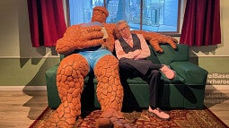 ben saunders pretending to sleep on a couch next to a life-sized marvel character figure