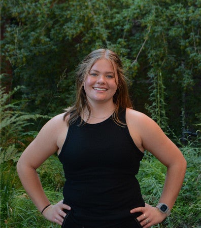 Laine Bell standing in front of green ivy, trees, and shrubs