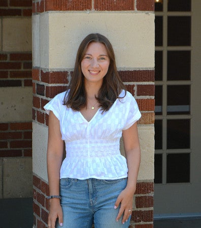 Maddy Carson standing in front of a marble and brick pillar.