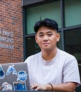 Head shot of Danny Nguyen behind his laptop outside the entrance to the Allan Price Science Commons and Research Library