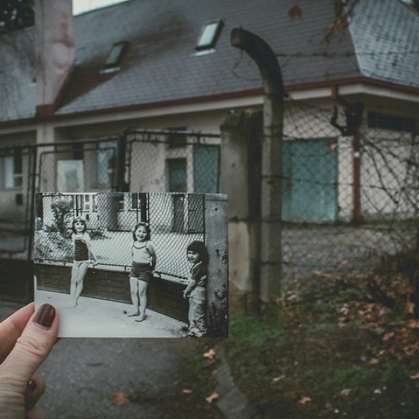 a black-and-white photo of three small children against a fence held up so that the photo matches up with the current fence behind the photo