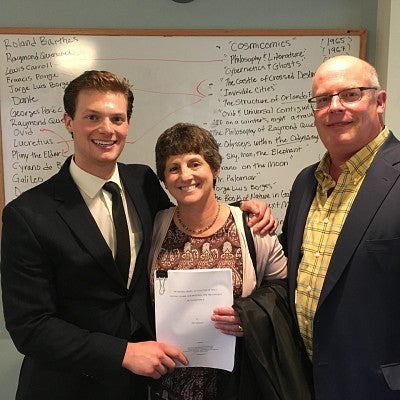 student and family in front of white board after defending thesis, with printed copy in hand