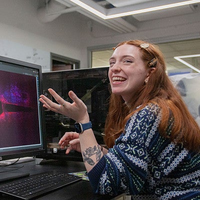avery suriano laughing while seated at lab computer with colorful science image on screen