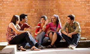 Five students sitting in front of a sunlit brick wall