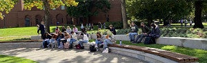 Students seated at an outdoor campus amphitheatre working on a class assignment