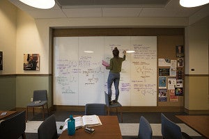 person standing on a chair while writing chemical equations on a white board