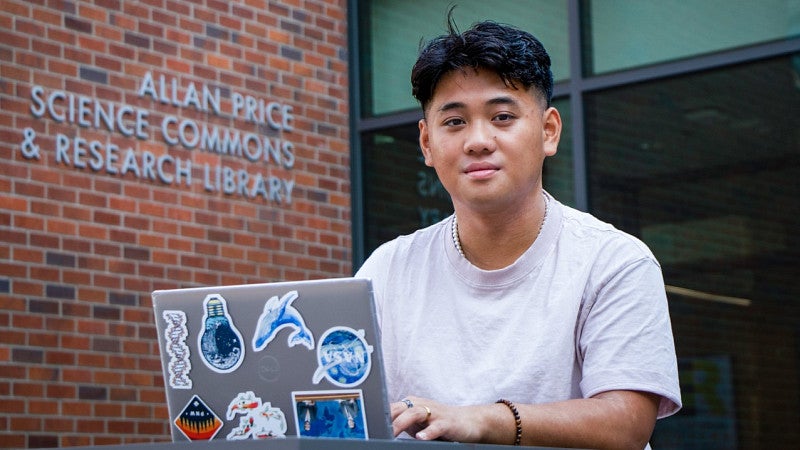 Head shot of Danny Nguyen behind his laptop outside the entrance to the Allan Price Science Commons and Research Library