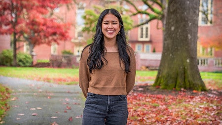 Alxis Shan standing in front of a campus tree with autumnal leaves