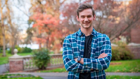 Landscape photo of Jon Laus, smiling and with arms crossed, standing outside in front of autumnal trees.