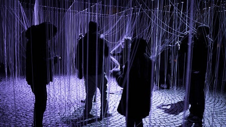 purple-toned photo of students walking through hanging strings