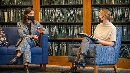 Two women, masked against COVID and socially distanced, discuss in the the Clark Honors College thesis library.