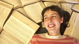 Smiling woman on the ground surrounded by many open reference books.