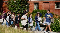A queue of students follows a peer advisor outside a campus building