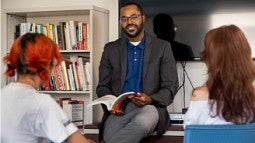 Marc Robinson sitting on a desk during office hours with two students