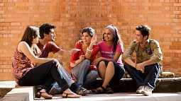 Five students sitting in front of a sunlit brick wall