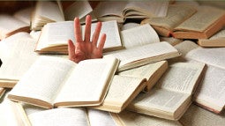 A left hand emerging from a pile of open books.