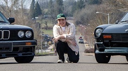 Anthony Cano kneals between two cars.
