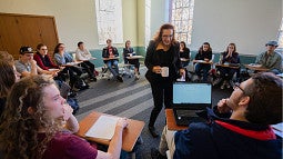 Students seated at desks in a ring around a female professor, who is asking a question.