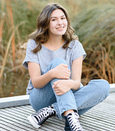 Abbi Biggs sitting cross-legged on a dock, grasses in the background.
