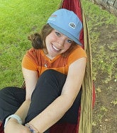 Analise Levy wearing a blue cap, red-and-orange shirt, and reclining in an orange hammock.  